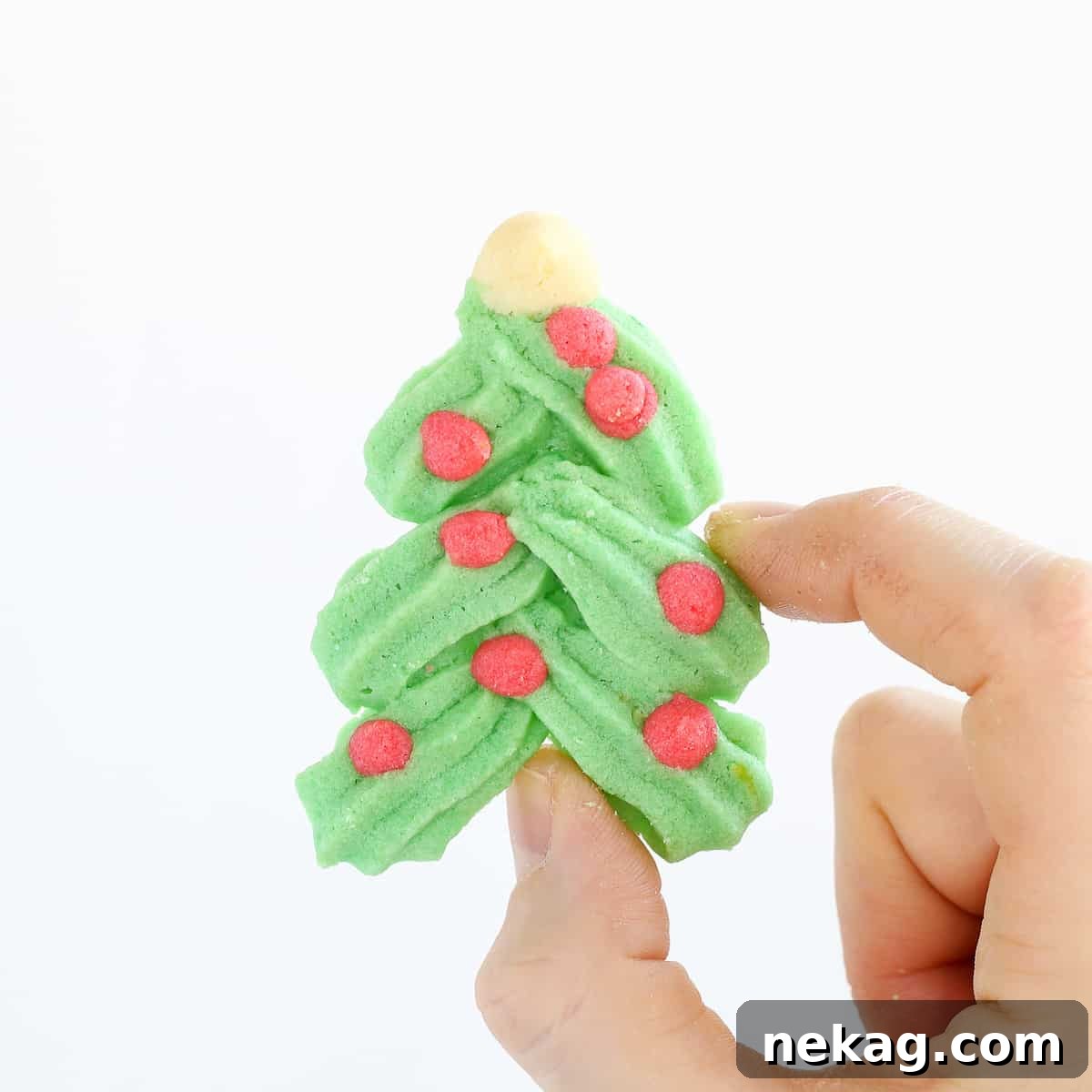 A festive Holiday Spritz cookie shaped like a Christmas tree, held delicately in hand.