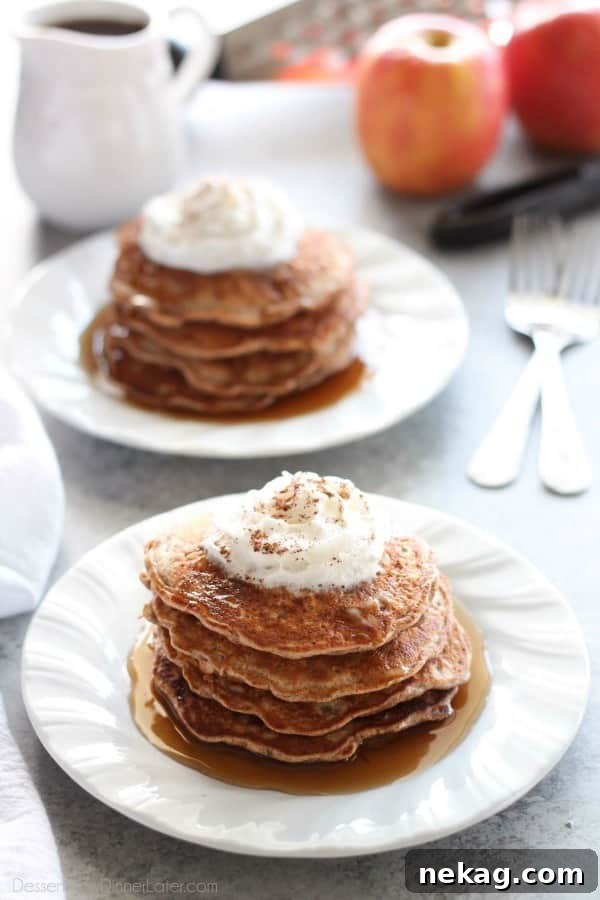 Fluffy Apple Cinnamon Pancakes stacked high with real apple pieces visible and a sprinkle of cinnamon, ready to be drizzled with syrup.