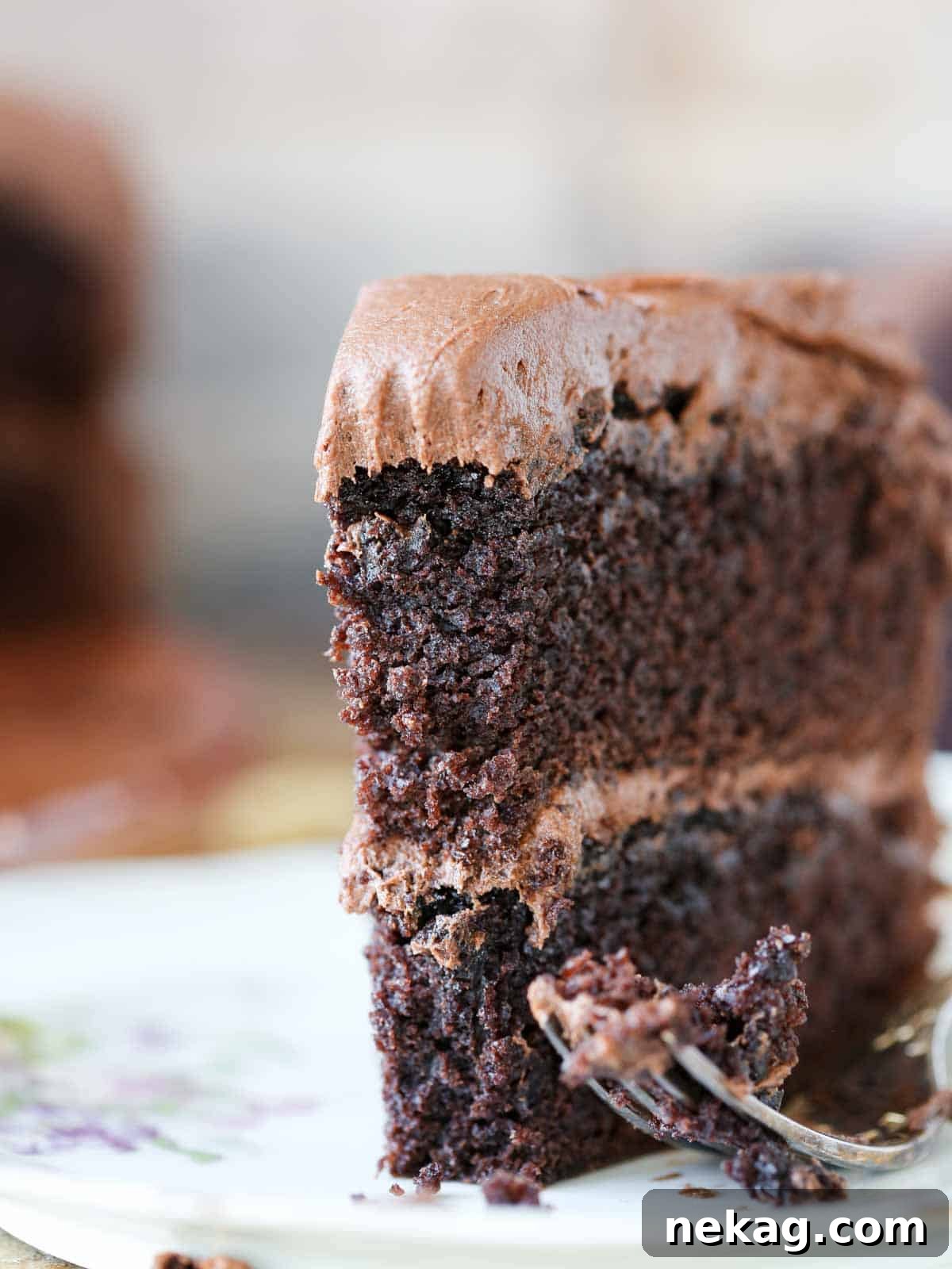 A perfectly sliced piece of moist chocolate cake, standing upright on a plate with a fork, showing its rich layers and creamy frosting.
