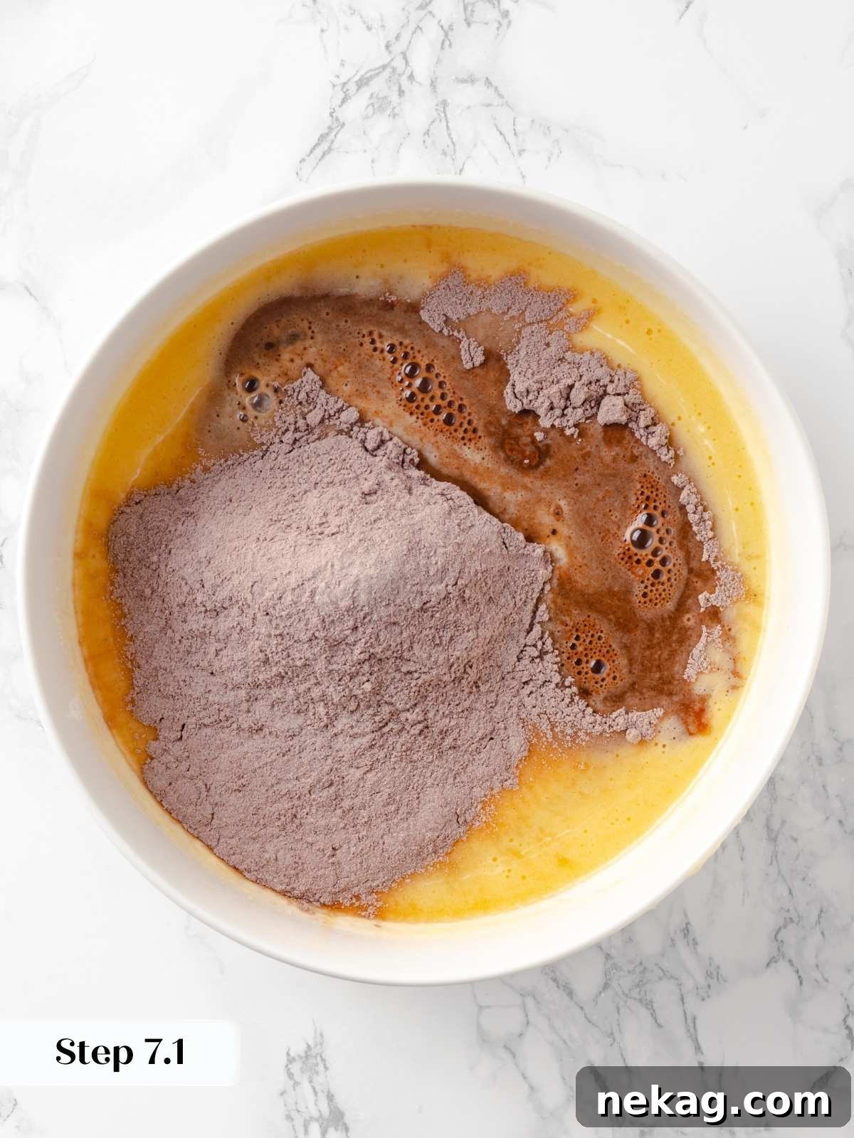 Dry ingredients are being gradually added to the large bowl of wet mixture, starting the formation of the cake batter.