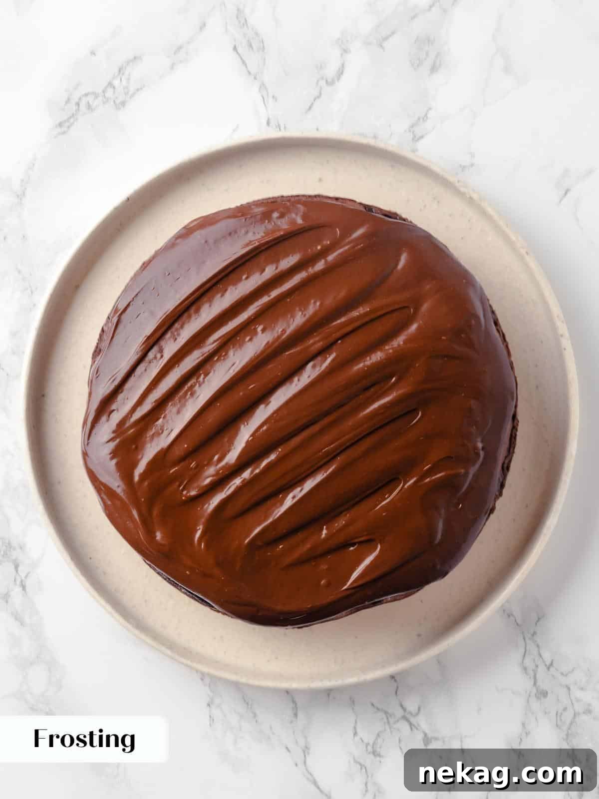 A thick, smooth layer of creamy chocolate frosting spread generously over the first cake layer, preparing for stacking.