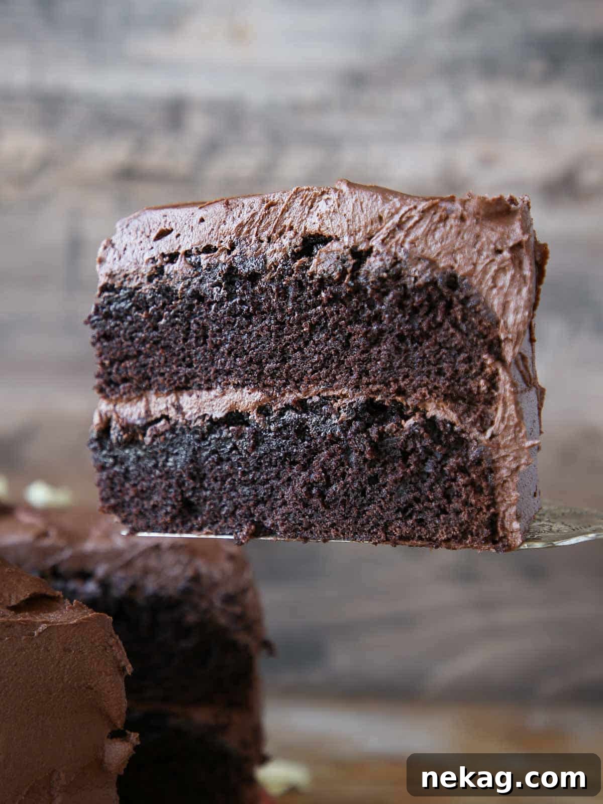 A hand serving a perfect slice of a beautifully layered chocolate cake, showing off its rich frosting and moist interior.
