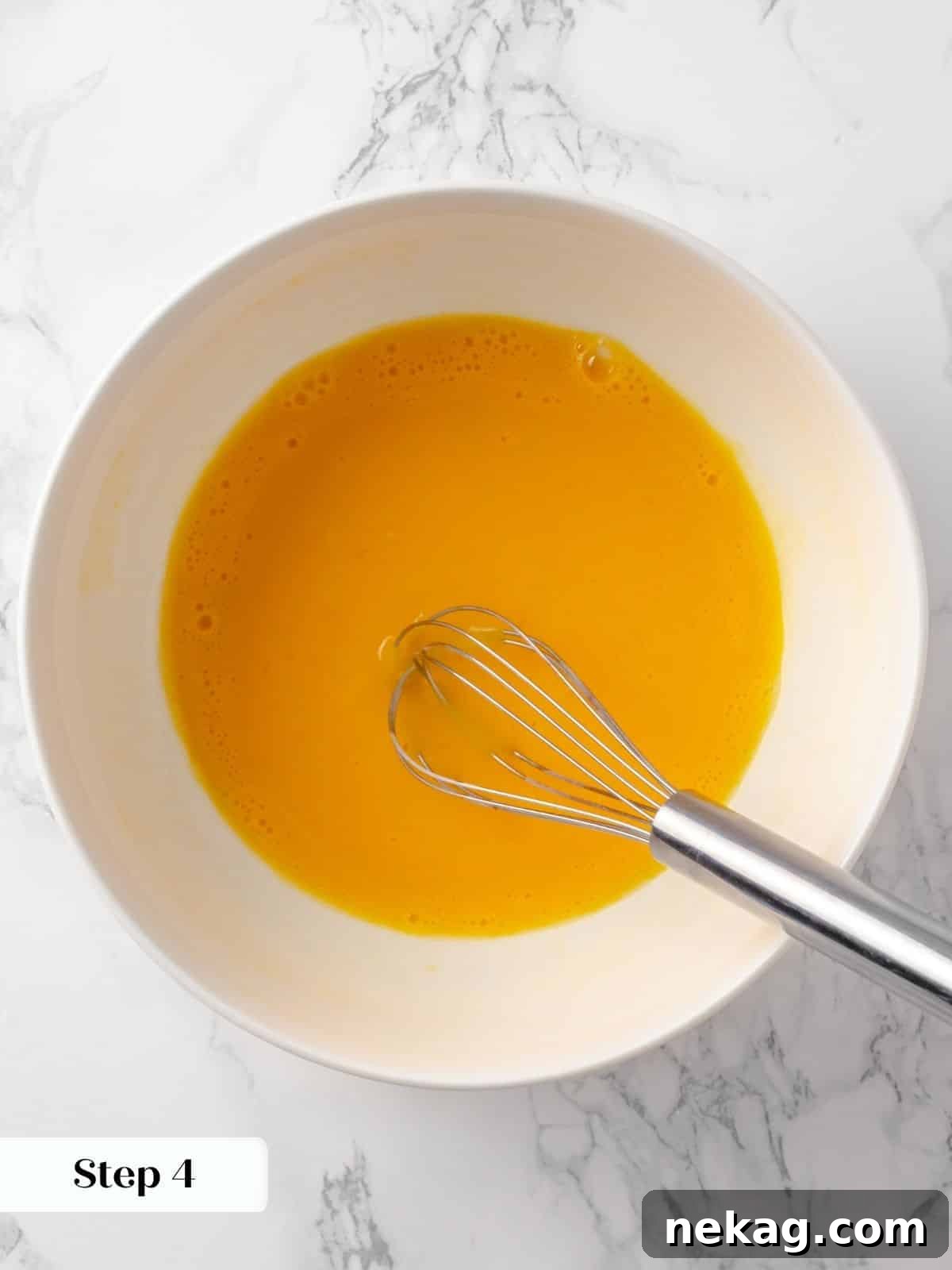 A large mixing bowl containing smoothly whisked wet ingredients, a golden and homogeneous mixture ready for the dry components.