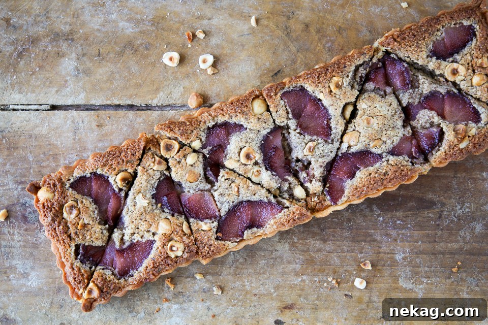 A slice of Hazelnut Pear Tart on a white plate, showcasing the layers of crust, frangipane, and red wine poached pears.