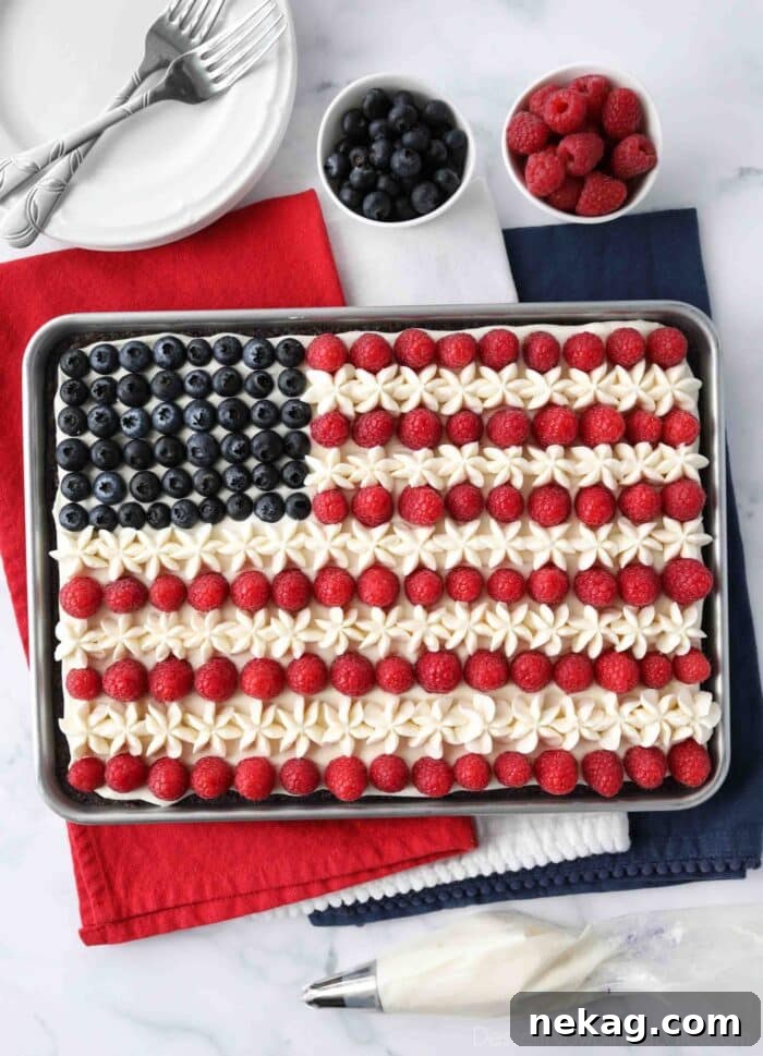 Overhead shot of a completed 4th of July Fruit Pizza, showcasing the full American Flag design with neat rows of raspberries and carefully placed blueberries on a creamy white frosting, all on a dark brownie base.