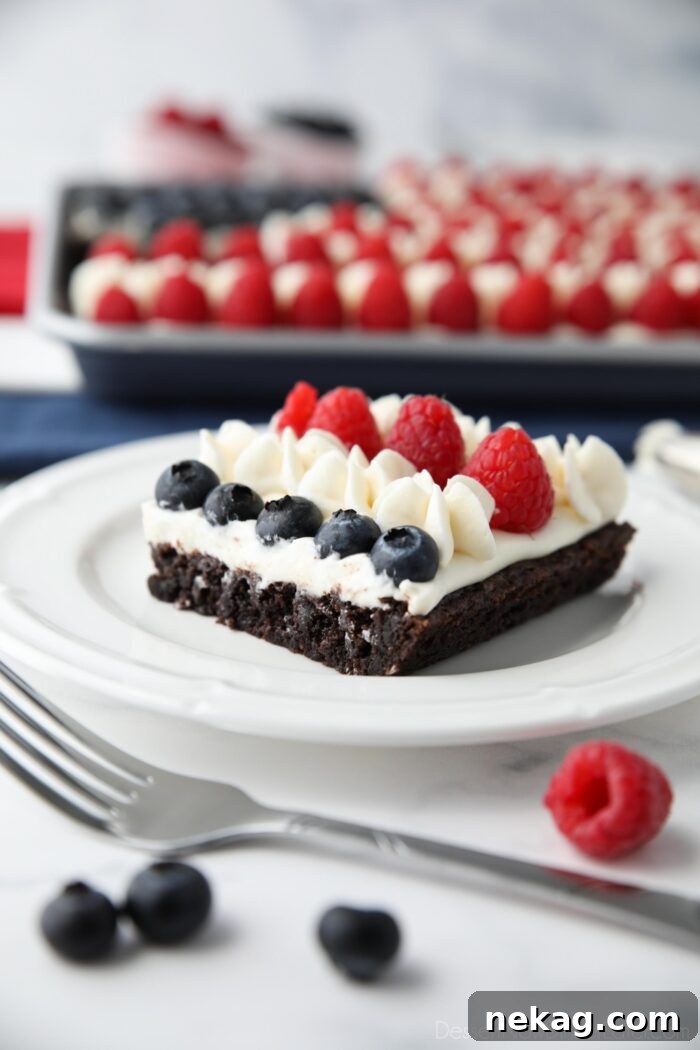 A single slice of the 4th of July Fruit Pizza presented on a white plate, highlighting the distinct layers of brownie, frosting, blueberries, and raspberries, ready to be enjoyed.