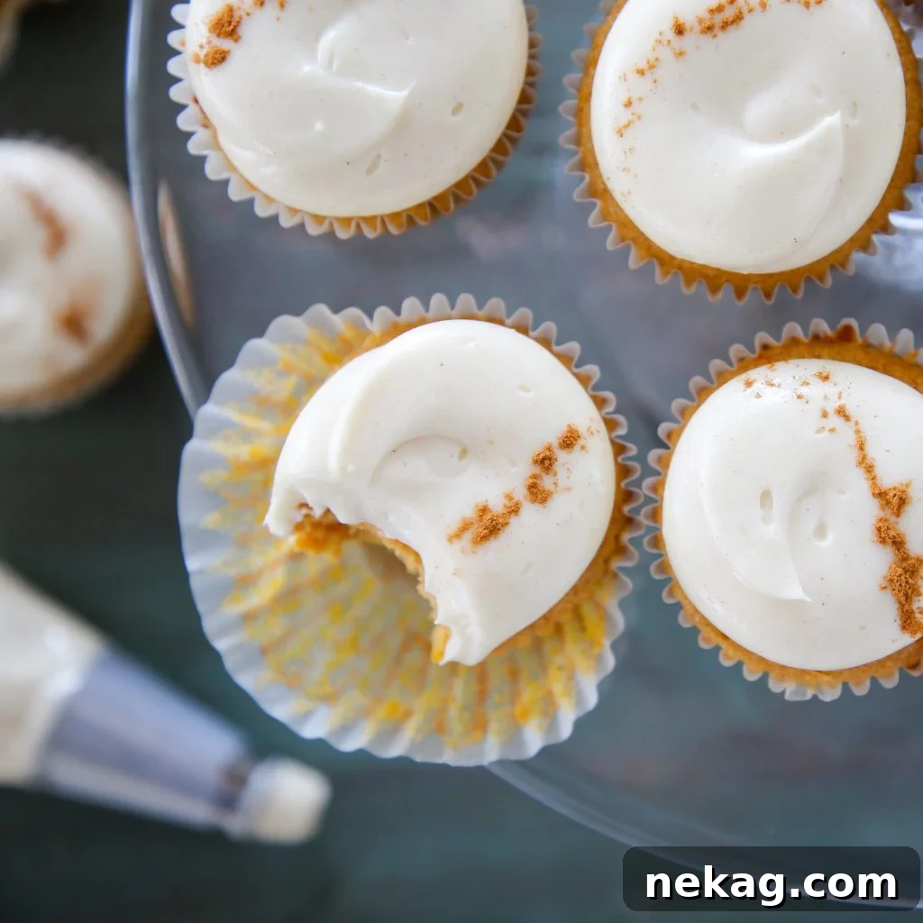 Decadent Pumpkin Cream Cheese Cupcakes 5 Two pumpkin spice cupcakes with maple cream cheese buttercream, one partially eaten, on a white plate with fall leaves