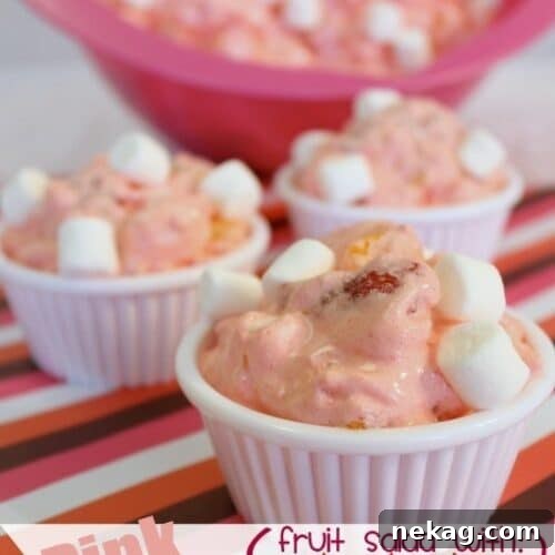 A close-up of Pink Fluff Fruit Salad in a serving bowl, garnished with fresh strawberries.