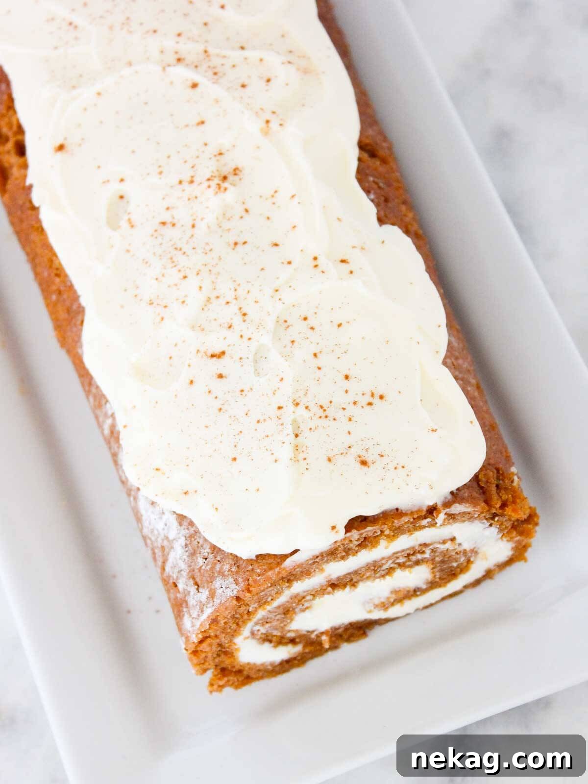 Heavenly Pumpkin Roll with Cream Cheese Filling 3 Beautifully textured unsliced pumpkin roll topped with a generous layer of creamy white cream cheese frosting, ready for chilling and serving.