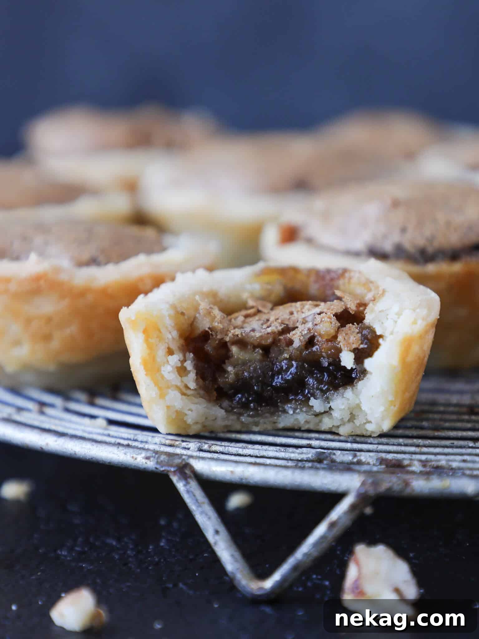 Delicious pecan tassies cooling on a wire rack, with one perfectly bitten to show the rich filling and flaky crust.