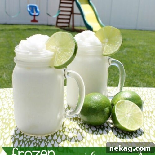 Two glasses of Frozen Coconut Limeade, garnished with lime, on a rustic wooden surface.