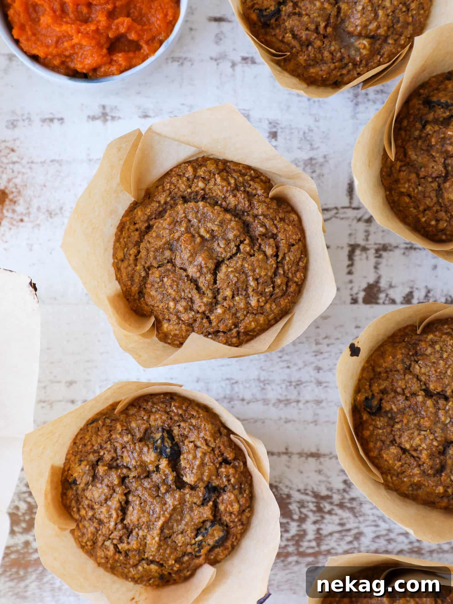 Wholesome Pumpkin Muffins 2 Freshly baked healthy pumpkin bran muffins arranged on a rustic white washed board, showcasing their golden-brown tops and inviting texture.