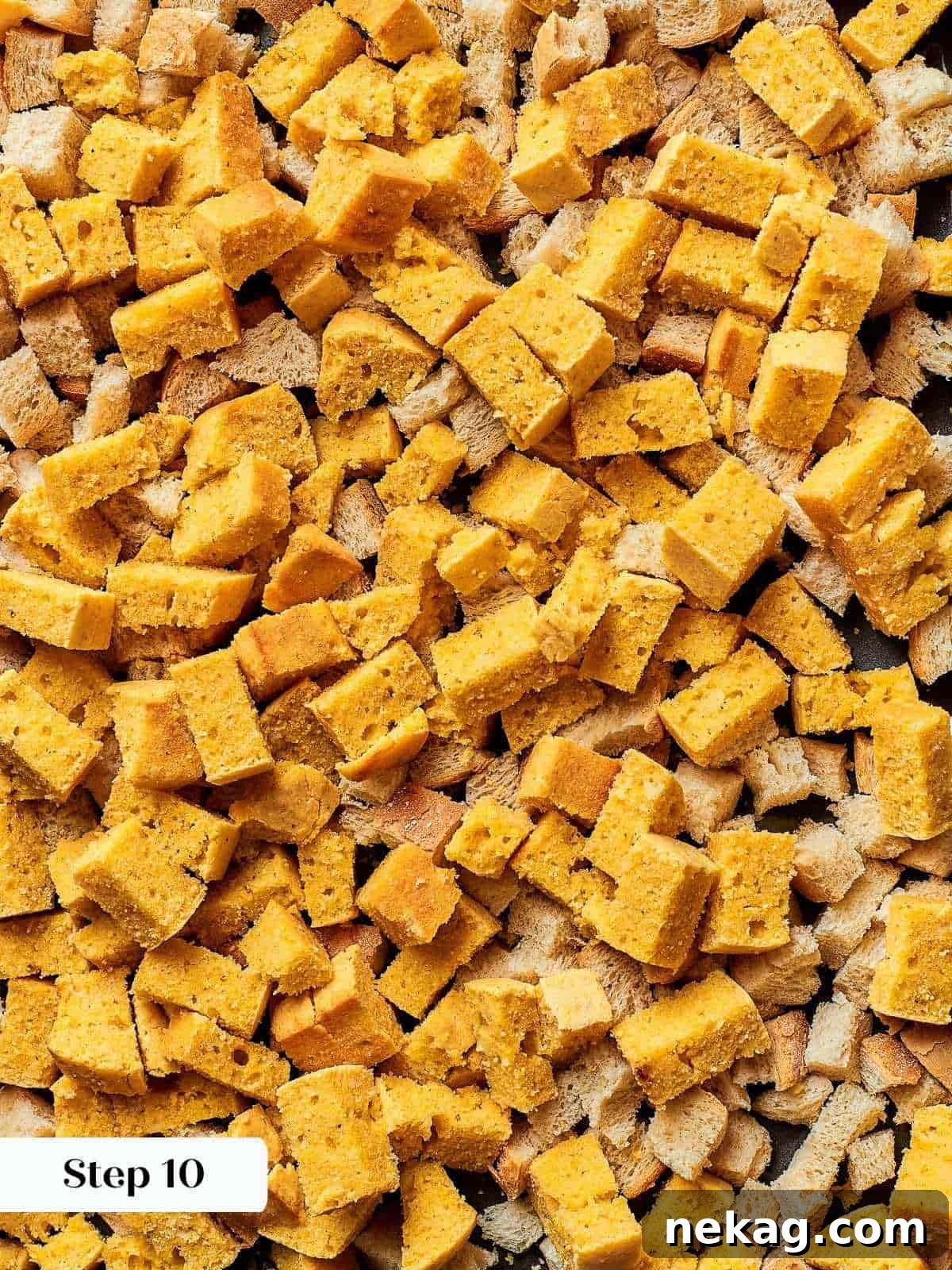 Cubes of cornbread and rustic French bread spread out on a baking sheet to dry overnight at room temperature, crucial for texture.