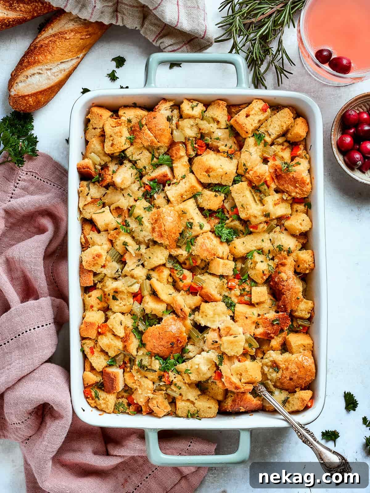 Baked cornbread dressing, golden brown and garnished with fresh rosemary, served alongside a sliced baguette on a rustic wooden table.