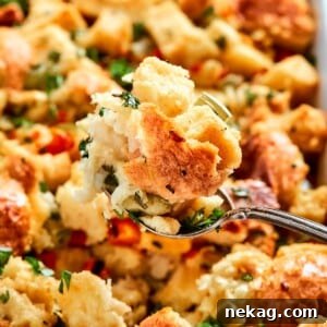 A spoon lifting a serving of Southern cornbread dressing, showcasing visible herbs and its moist, golden crumb texture.