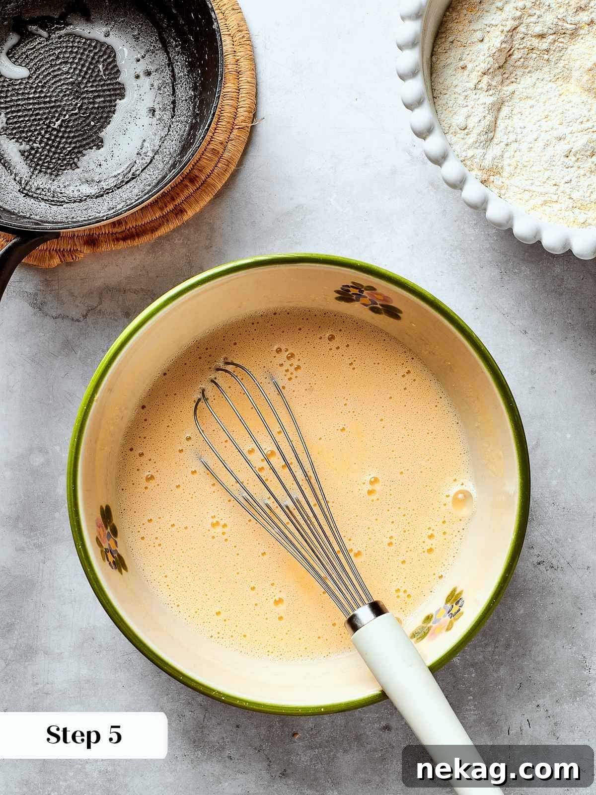 Milk being gradually whisked into beaten eggs in a bowl, creating a smooth wet mixture for the cornbread.