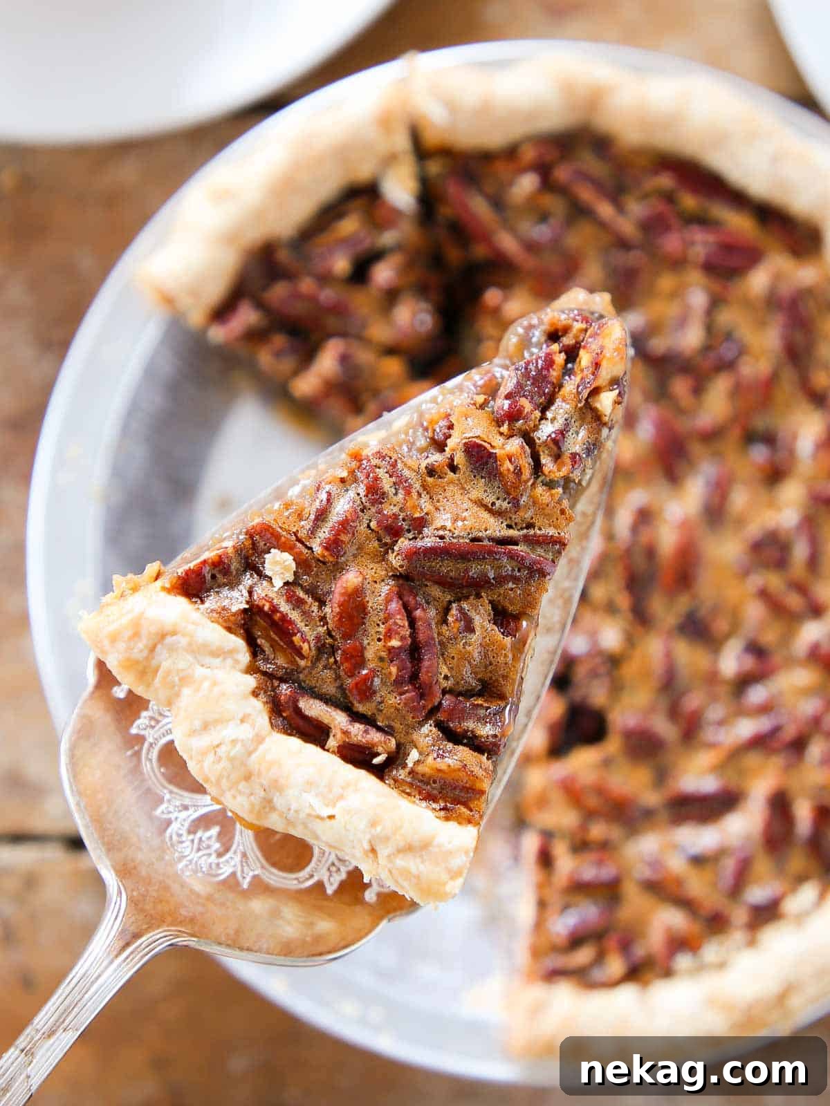 Decadent Pecan Pie Perfection 2 A delectable slice of pecan pie on a server, showcasing its rich filling and golden crust, poised above a whole, freshly baked pecan pie.