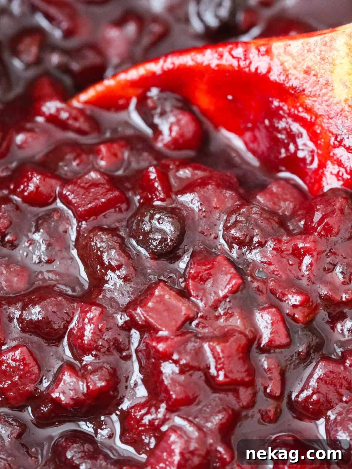 Festive Cranberry Relish 2 Vibrant cranberry chutney served up close on a rustic wooden spoon, showcasing its rich texture and festive color against a warm wooden background.