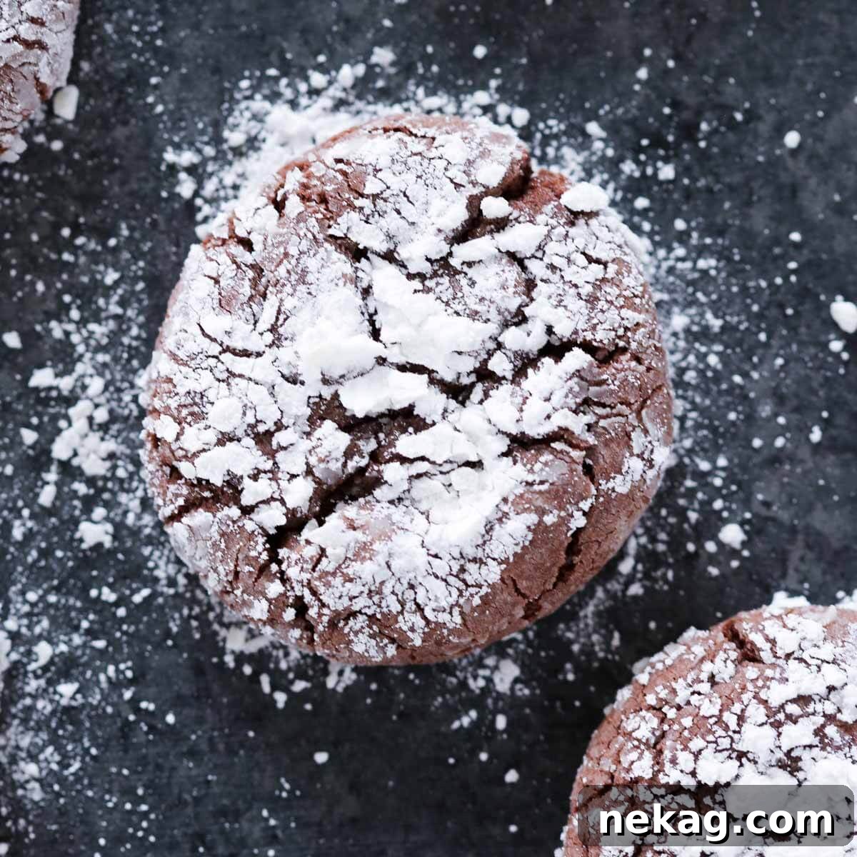 A perfectly baked chocolate crinkle cookie with distinct powdered sugar cracks on a dark surface, showcasing its festive appearance.