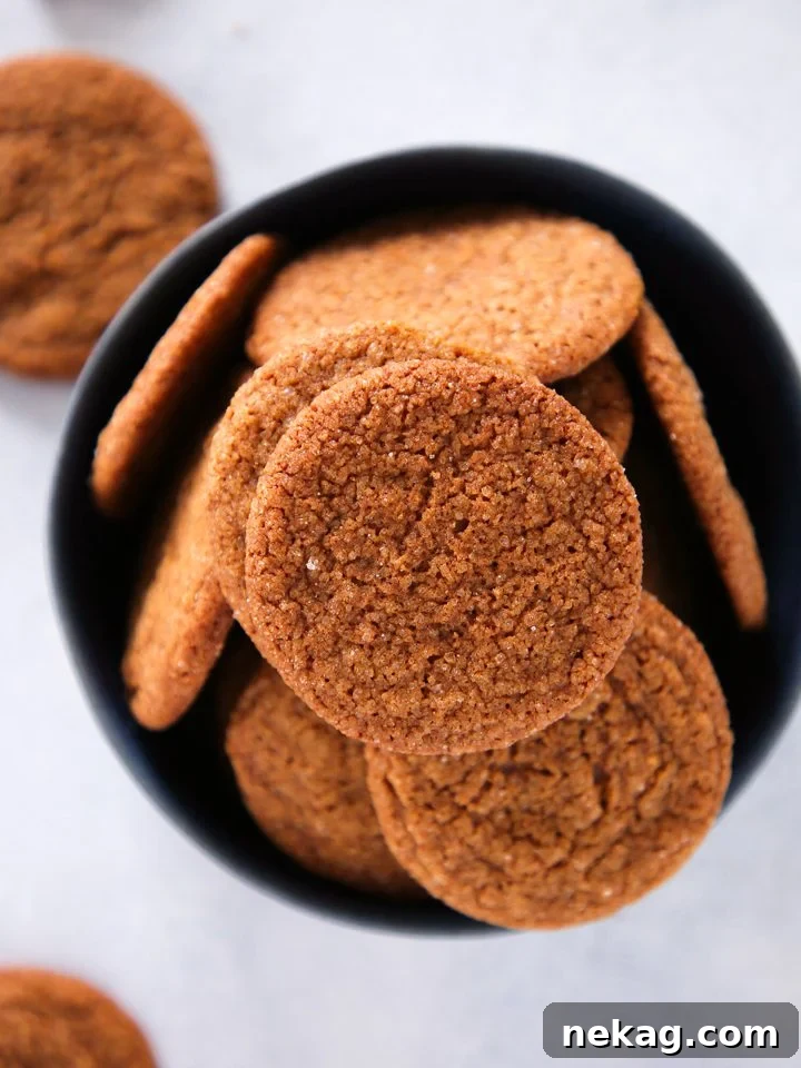 Close-up of three Old Fashioned Gingersnaps on a light wooden surface, showcasing their sugary crust and inviting texture, ready to be enjoyed.