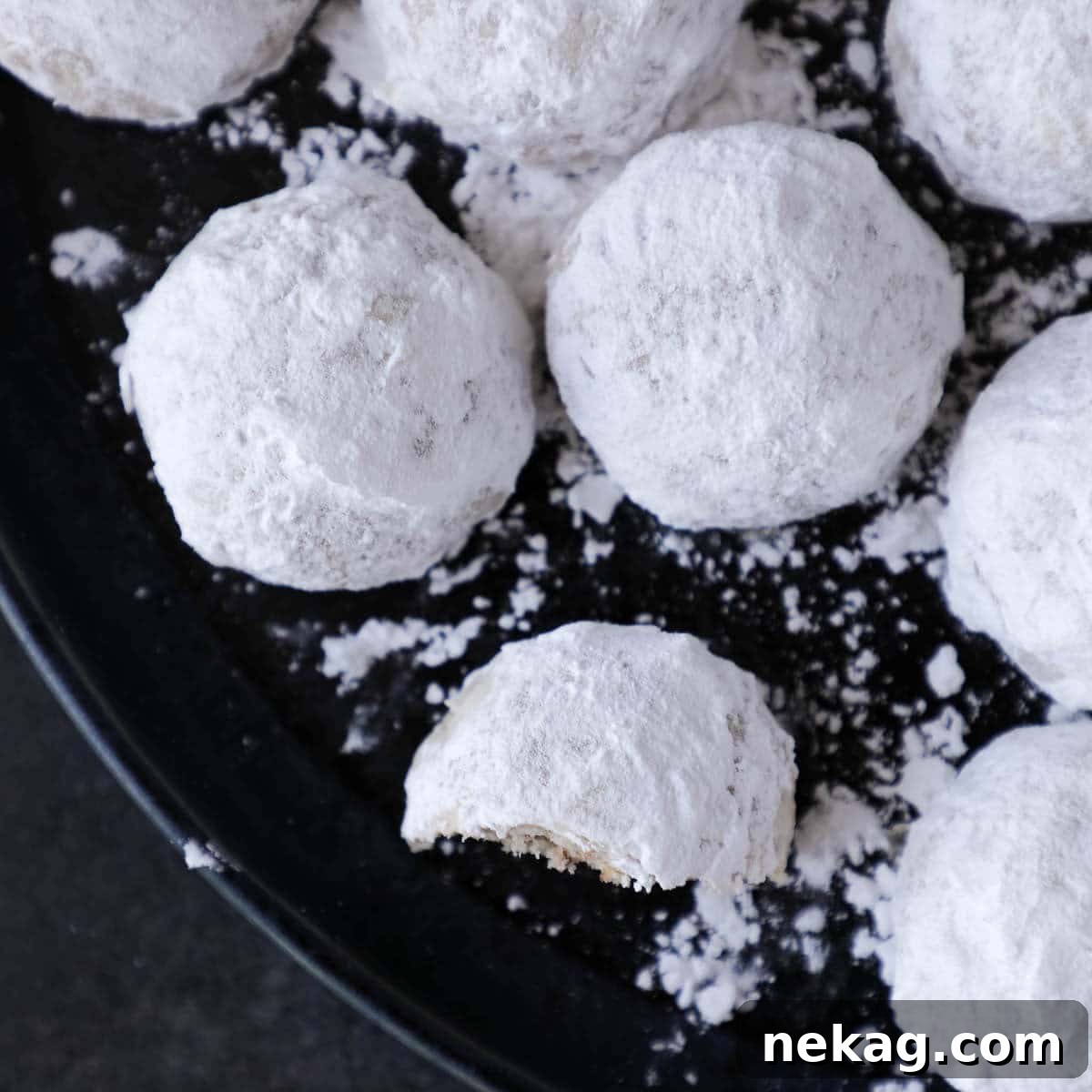 Buttery Pecan Snowball Bites 3 A beautiful arrangement of pristine white snowball cookies, generously coated in powdered sugar, resting on a sophisticated black plate, ready for serving.