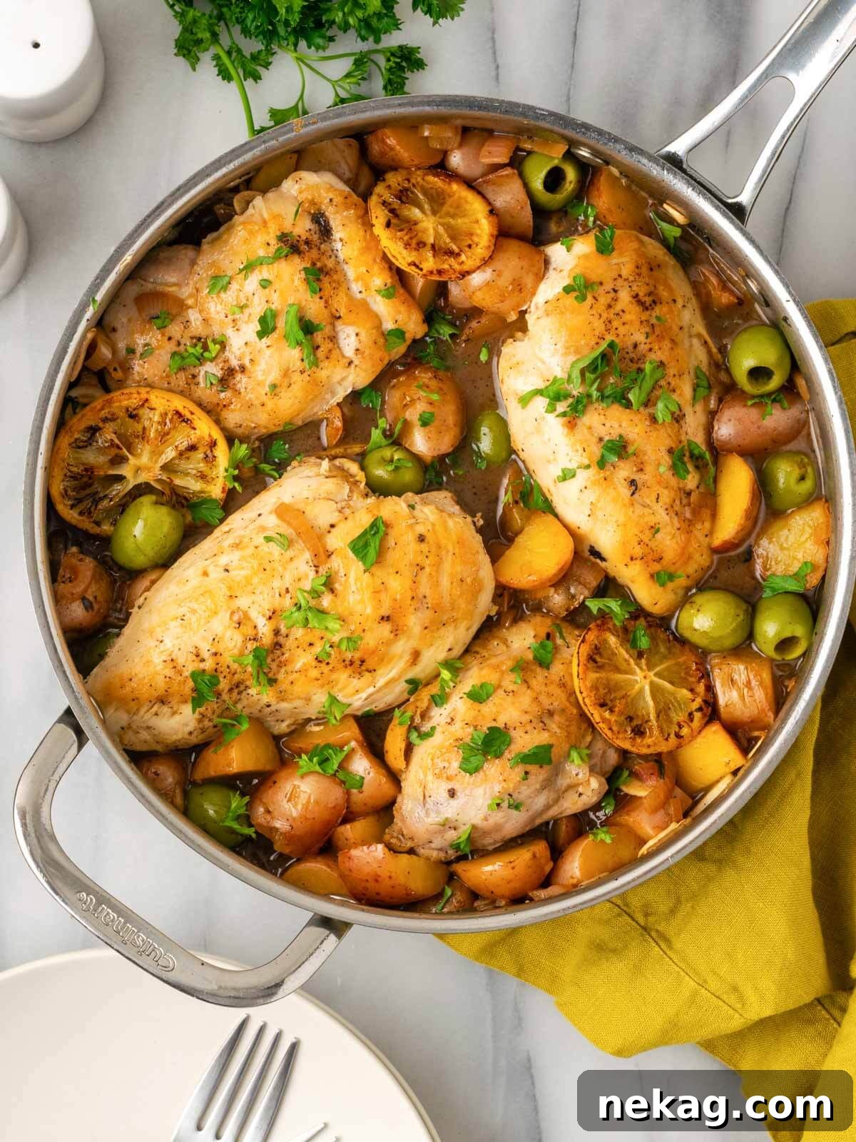 Golden brown lemon chicken and potatoes in a skillet, garnished with fresh parsley and lemon slices, resting on a marble surface.