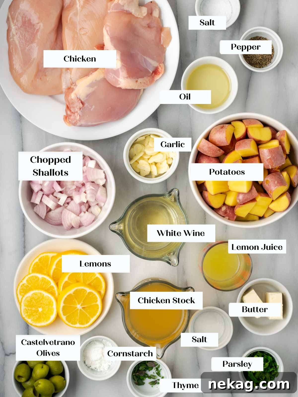 Fresh ingredients for lemon chicken arranged on a marble counter, including chicken, lemons, potatoes, garlic, shallots, and herbs.
