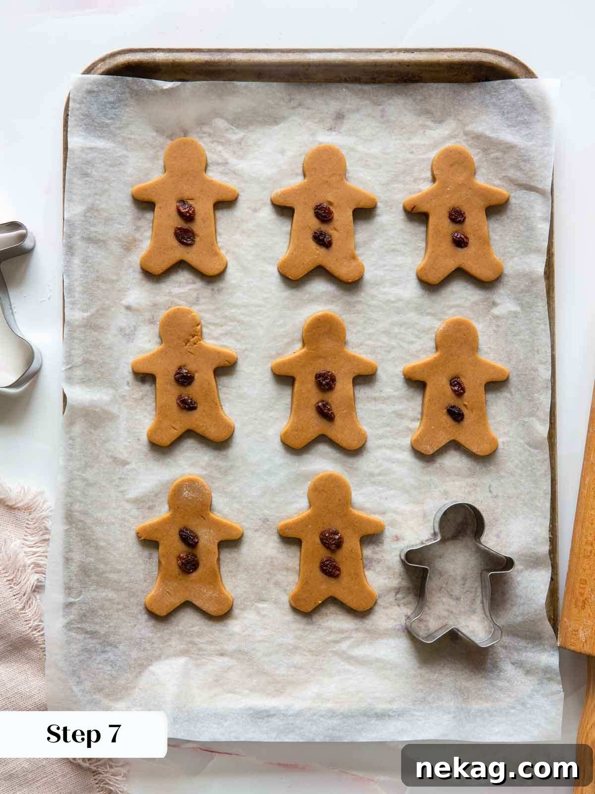 Raw gingerbread cookies, shaped like gingerbread men, being adorned with small raisins before they are baked, adding a personal and tasty touch.