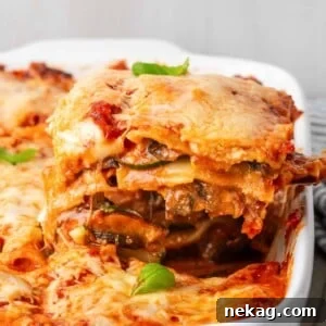 A slice of vegetable lasagna being pulled from the pan, showing an impressive cheese pull with gooey mozzarella.