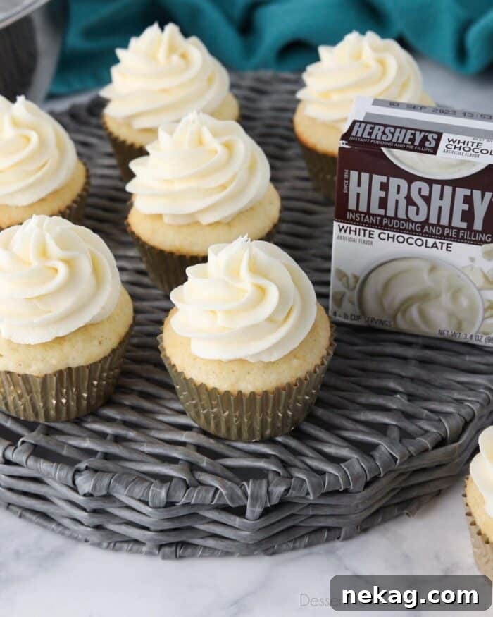 Delicious Pudding Buttercream Frosting Recipe 4 Close up top view of white chocolate pudding frosting on top of white cupcakes and a box of Hershey's instant pudding.