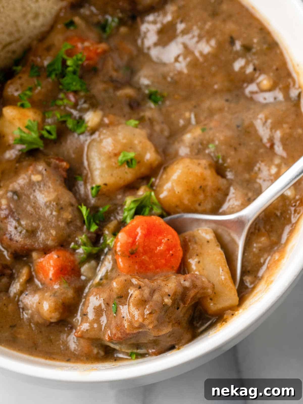 Closeup of hearty beef stew on a spoon, showcasing tender meat and vegetables.