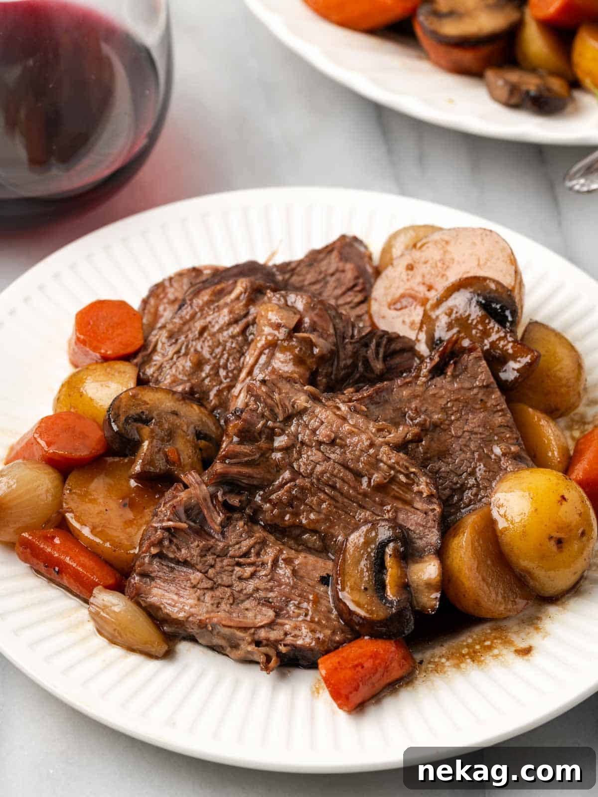 sliced pot roast with tender vegetables on a white plate, ready to serve.