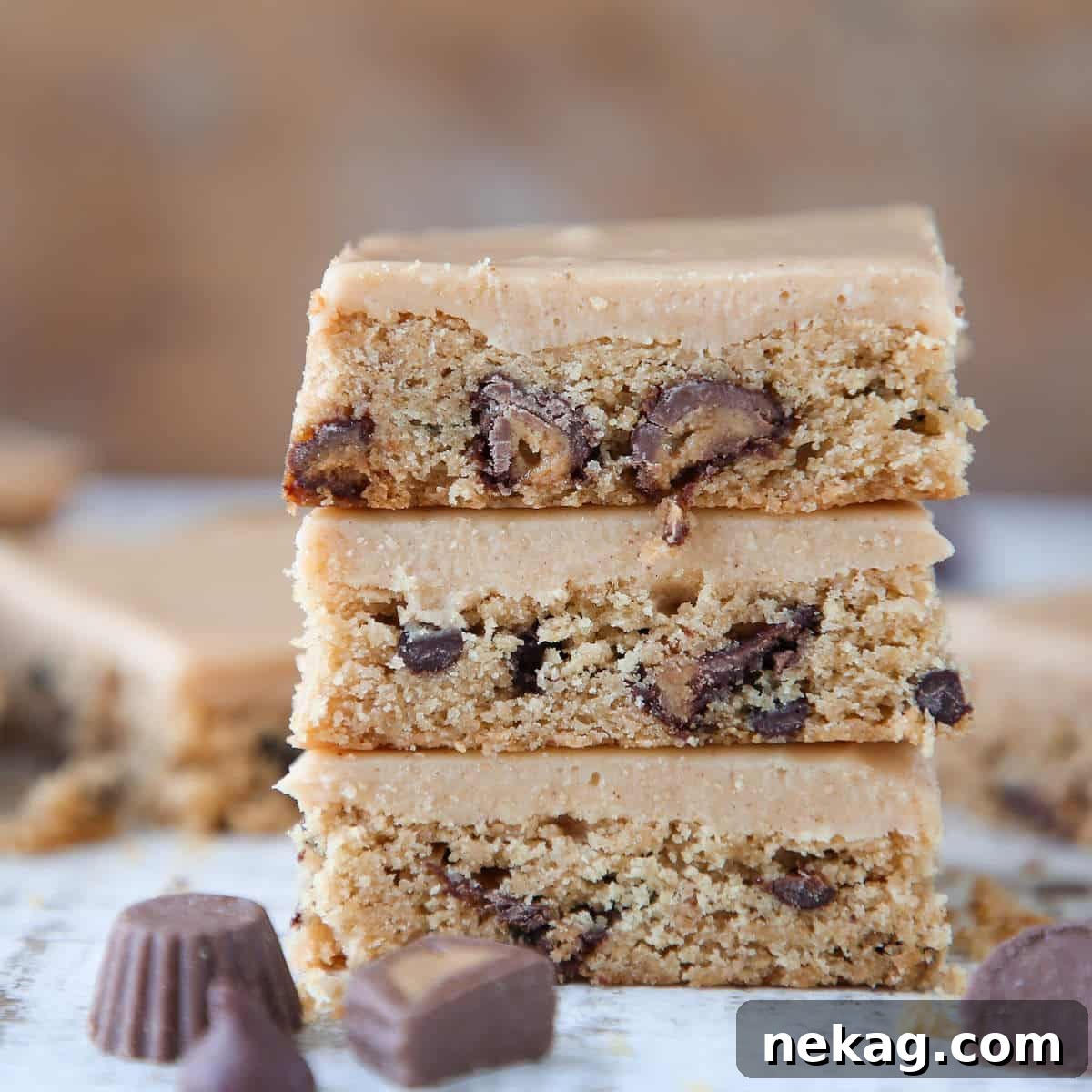 Ultimate Reeses Peanut Butter Blondies 5 A stack of three Reese's Peanut Butter Blondies, freshly sliced, with visible layers of frosting and embedded chips.