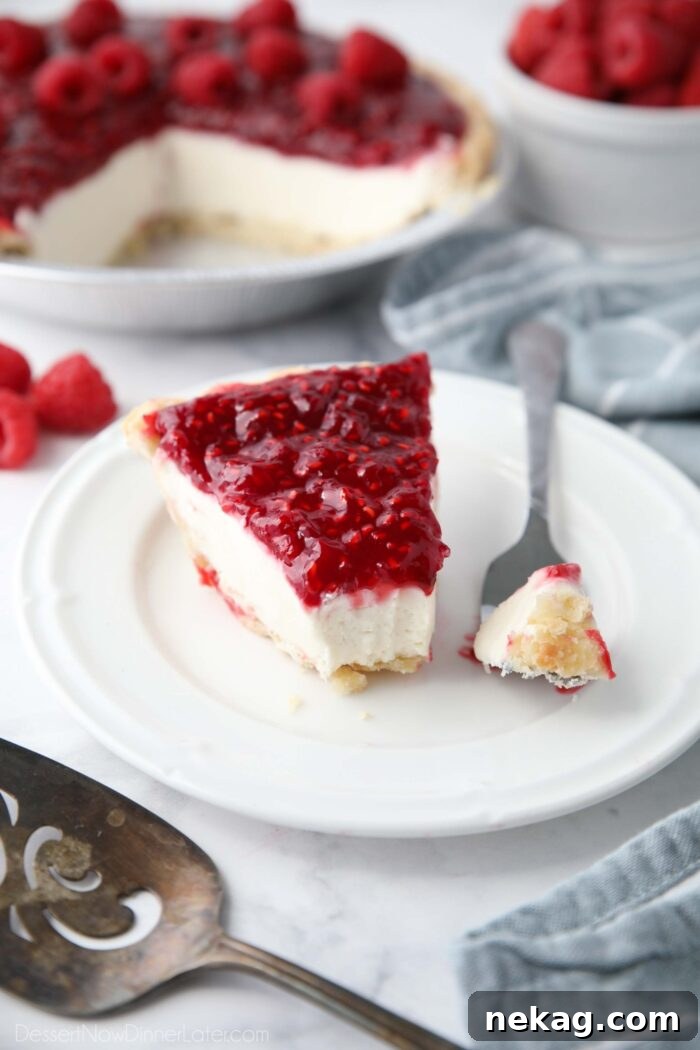 Slice of Raspberry Cream Pie on a plate with a forkful taken out to show layers of pastry crust, whipped cream cheese filling, and raspberry topping.