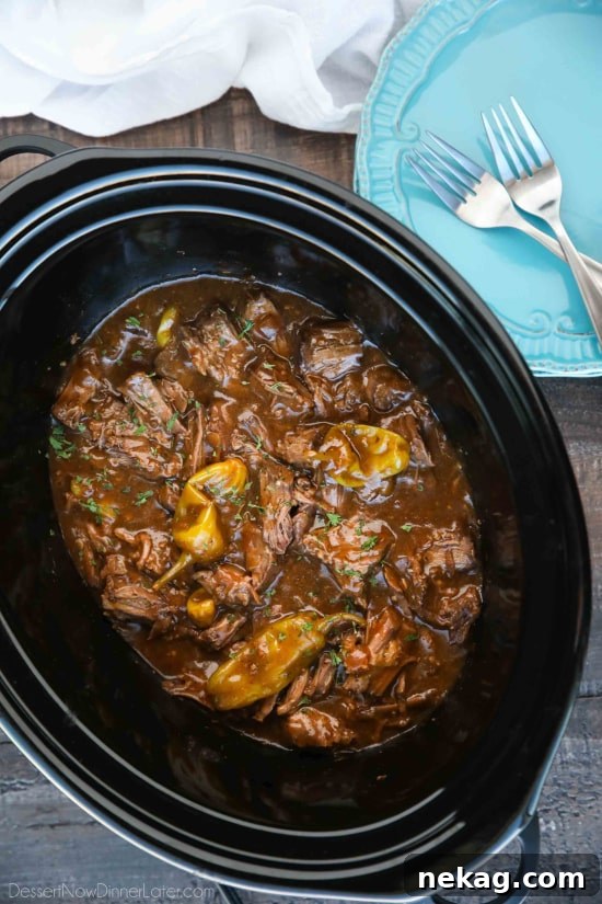 Slow cooker filled with deliciously shredded Mississippi Pot Roast simmering in its rich gravy.