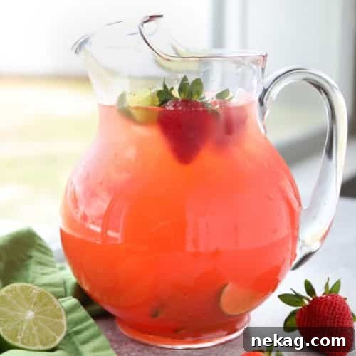 A close-up of a glass of Strawberry Agua Fresca, garnished with a lime slice and whole strawberry.