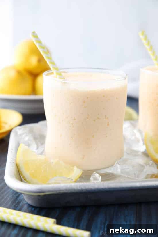 Two glasses of frosted lemonade, one with a straw and lemon slice, showcasing the thick, frothy texture, ready to be enjoyed on a sunny day.