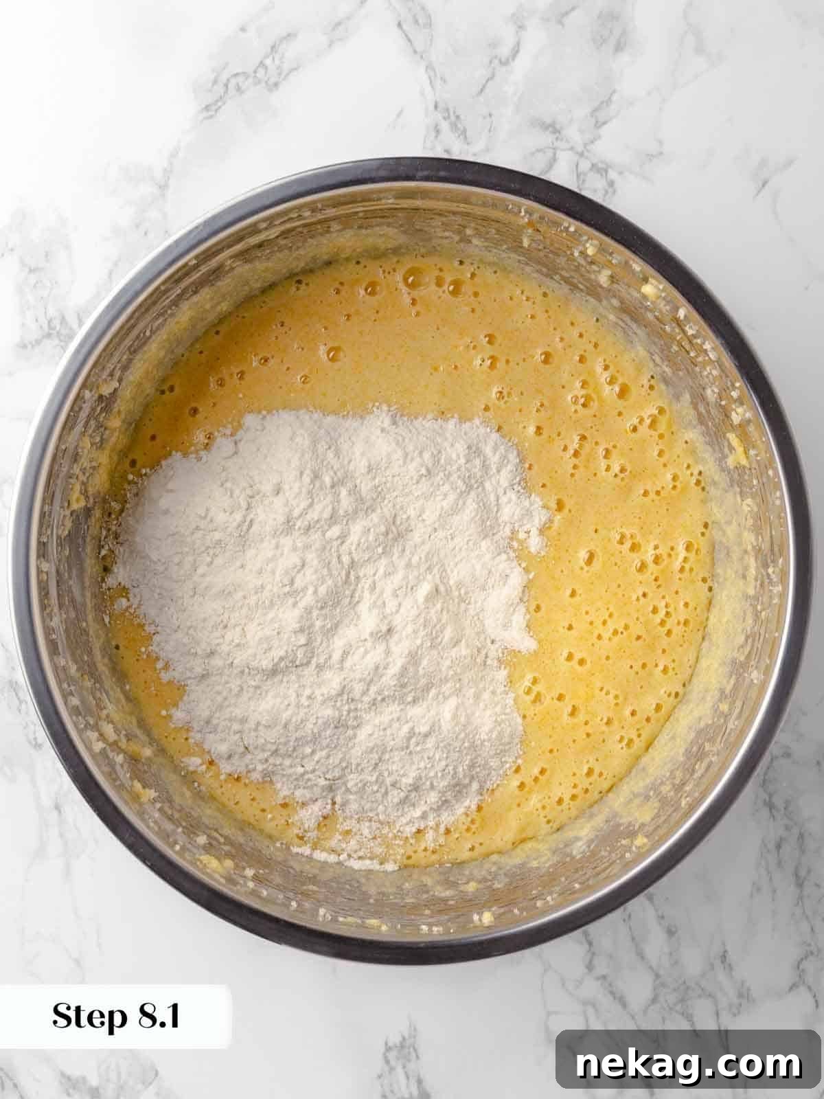 Flour being gradually added to the rich chocolate cupcake batter in a stand mixer, alternating with liquid ingredients to create a smooth batter.