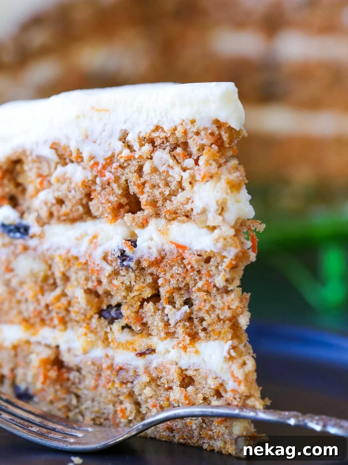A side view of a beautifully frosted three-layer carrot cake, showcasing its moist texture.