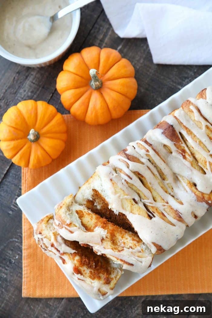 A freshly baked loaf of Pumpkin Pull Apart Bread, golden brown and glistening with a smooth cream cheese glaze, invitingly placed for a fall breakfast or dessert.