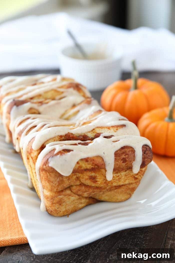 A close-up view of a slice of Pumpkin Pull Apart Bread, showing the intricate layers of soft yeast dough separated by sweet and spiced pumpkin filling, topped with a generous swirl of cream cheese frosting.