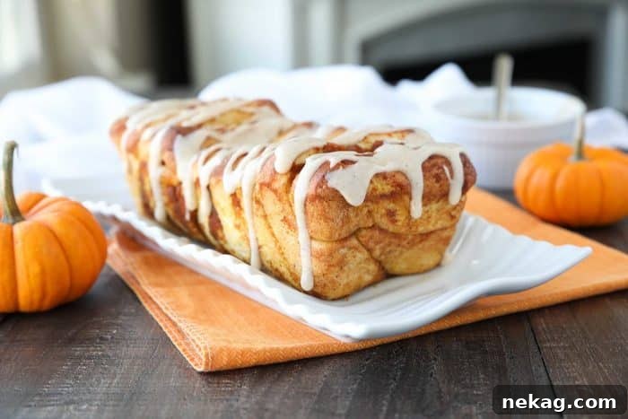 A stunning shot of a complete Pumpkin Pull Apart Bread loaf, beautifully glazed and presented, highlighting its inviting, ready-to-be-pulled-apart layers on a rustic wooden board.