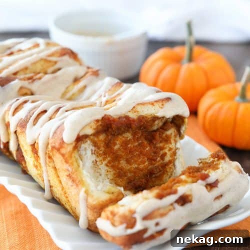 A beautifully presented loaf of Pumpkin Pull Apart Bread with visible layers of pumpkin and spices, topped with a creamy white glaze, ready for serving.