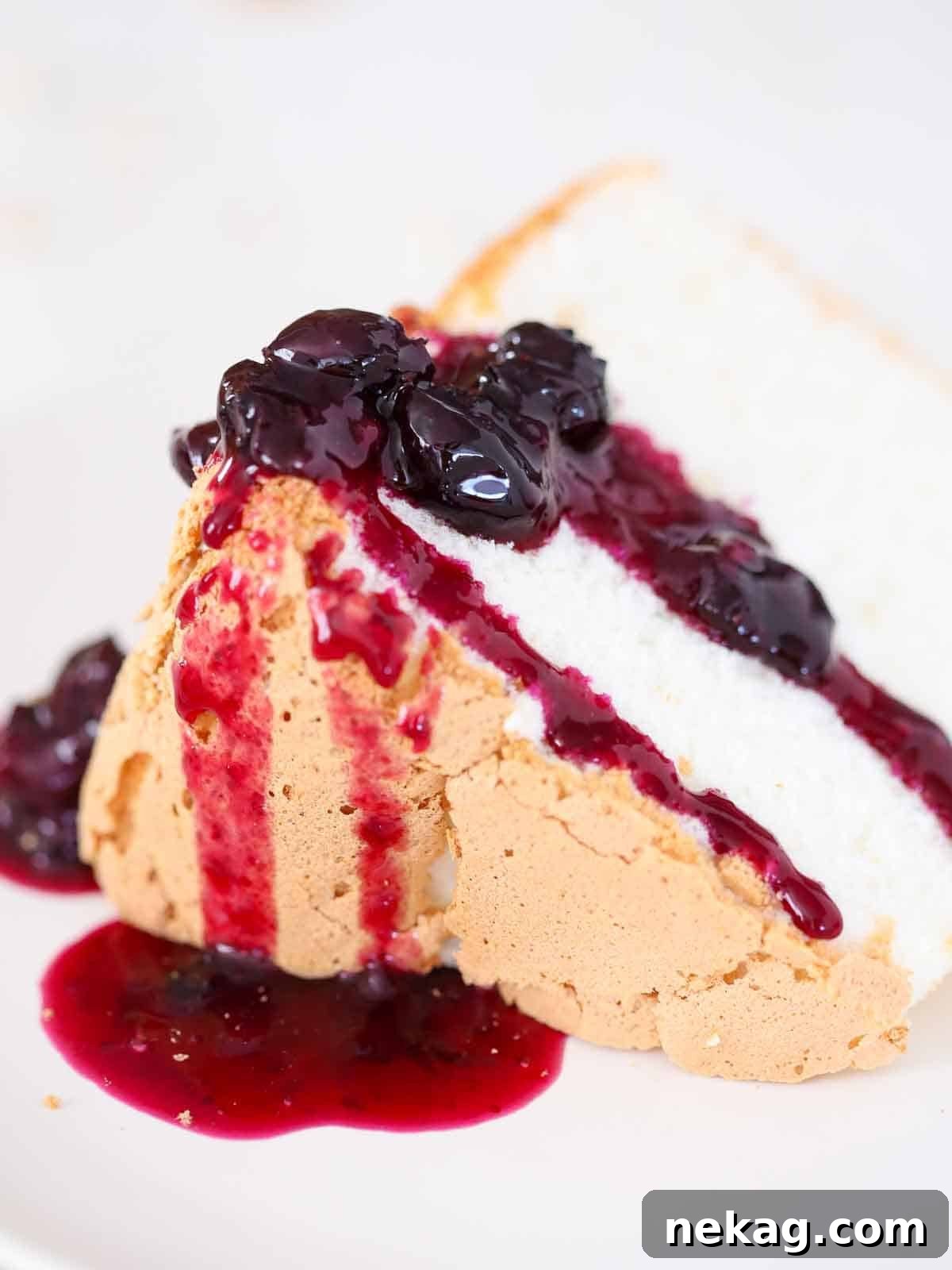 Whisper-Light Delight 3 A slice of angel food cake adorned with vibrant blueberry sauce, artfully pooled on a white plate.