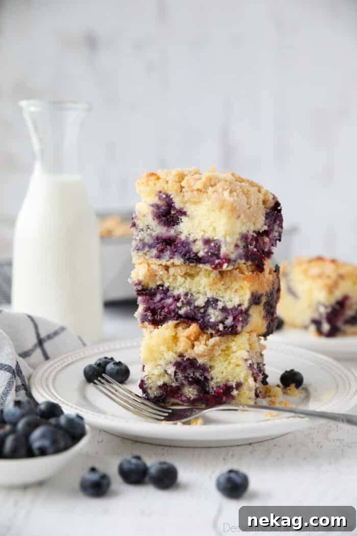 Three perfectly cut slices of homemade blueberry coffee cake, stacked invitingly on top of each other, ready to be enjoyed.