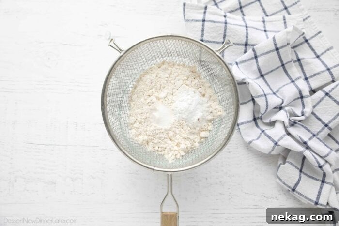 Dry cake ingredients being sifted through a fine mesh sieve into a mixing bowl.