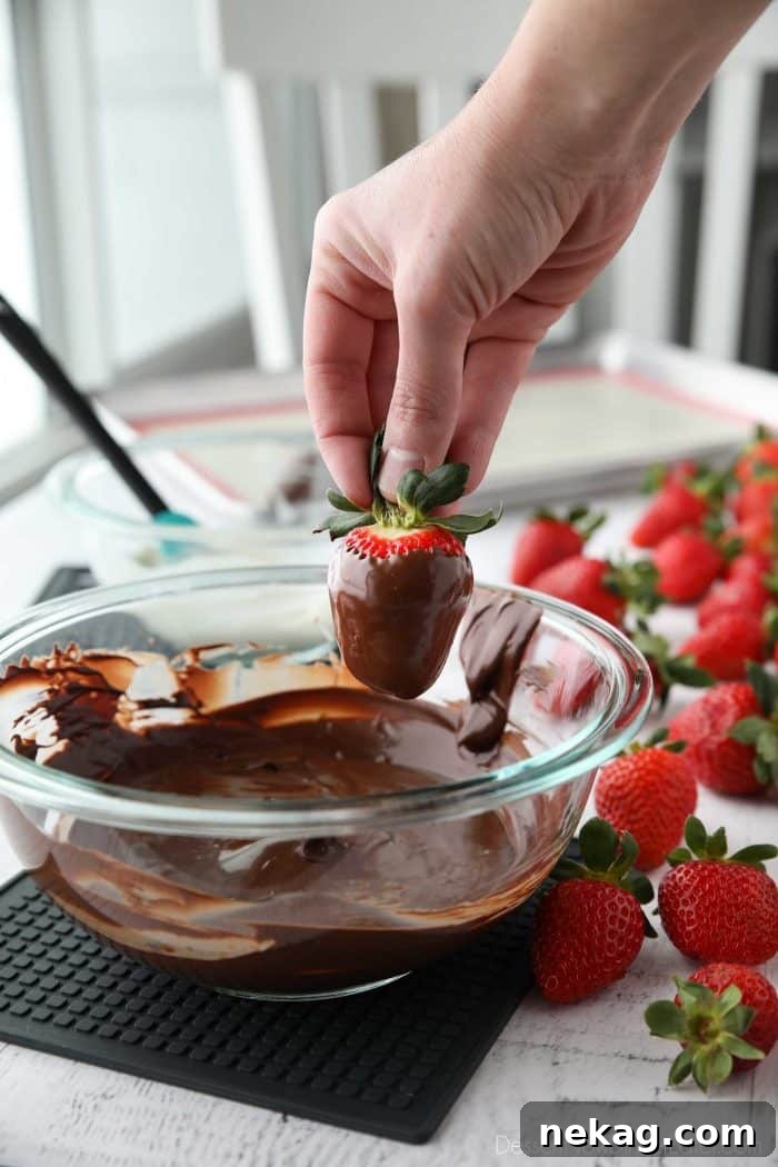 To dip a strawberry in chocolate: Hold the strawberry firmly by the stem, dip it into the melted chocolate, twist/rotate the berry until fully coated, then let the excess chocolate fall back into the bowl, or lightly scrape the bottom on the side.