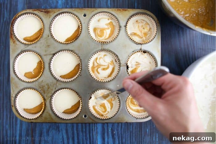 Detailed shot of assembling Pumpkin Cream Cheese Muffins: pumpkin muffin batter on the bottom, cheesecake batter on top, ready to be folded with a knife for a swirled look