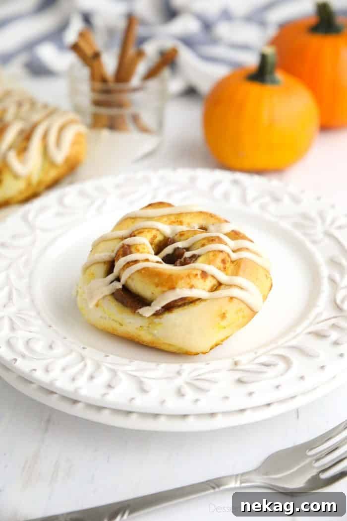 Pumpkin Pie Spiced Cinnamon Rolls 2 A Pumpkin Pie Cinnamon Roll on a plate with decorative pumpkins and cinnamon sticks in the background, hinting at autumn.