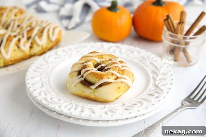 Pumpkin Pie Spiced Cinnamon Rolls 12 A single Pumpkin Pie Cinnamon Roll on a white plate, artfully arranged with small decorative pumpkins and cinnamon sticks in the background.